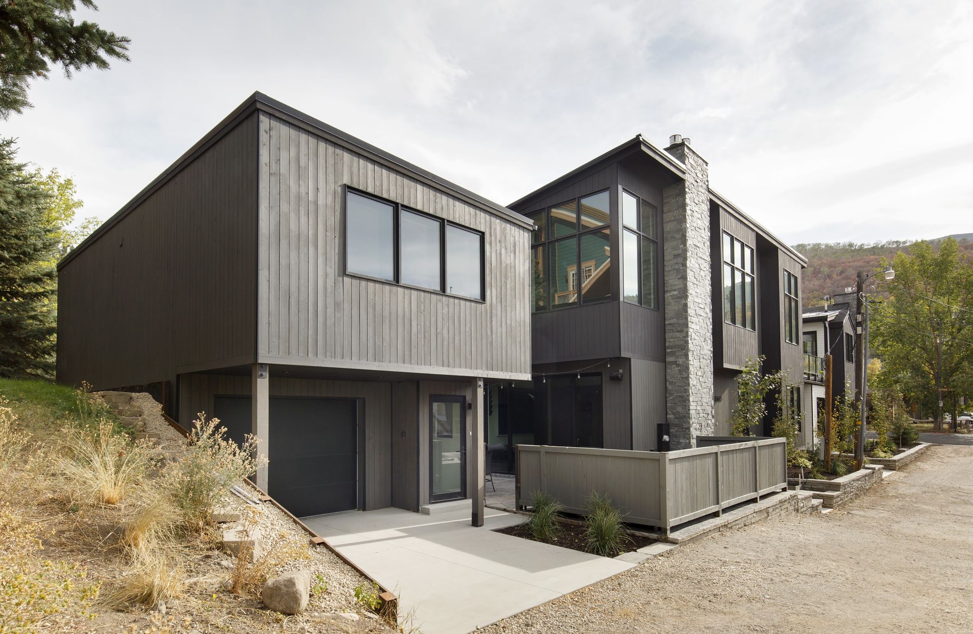 Front of SkiHome, 1064 Park Avenue Unit B: charcoal board-and-batten siding, stacked stone chimney and black-framed windows under autumn aspens in Old Town Park City