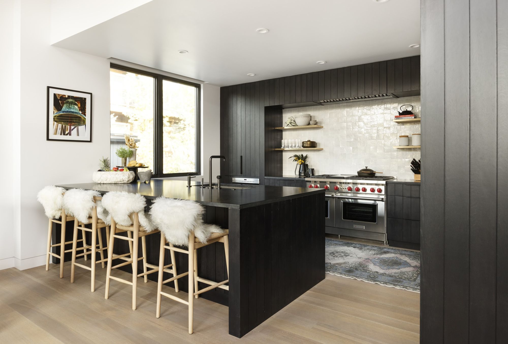 Kitchen with black cabinetry, island seating for four and Wolf range